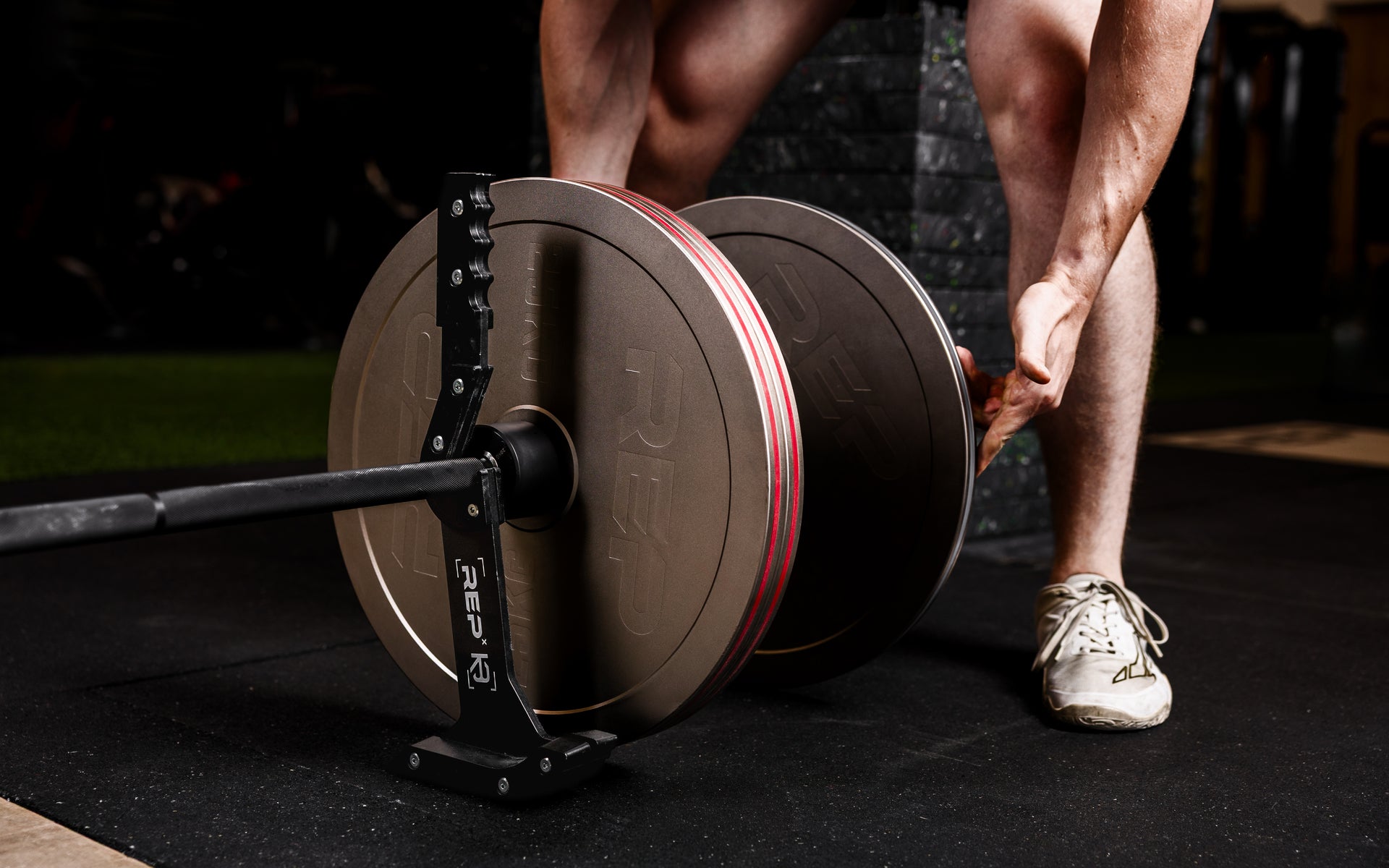 Athlete loading Rep Fitness Calibrated Steel Plates (KG) onto a barbell using the REP® x Kleva Built® Genesis Jack® 2.0